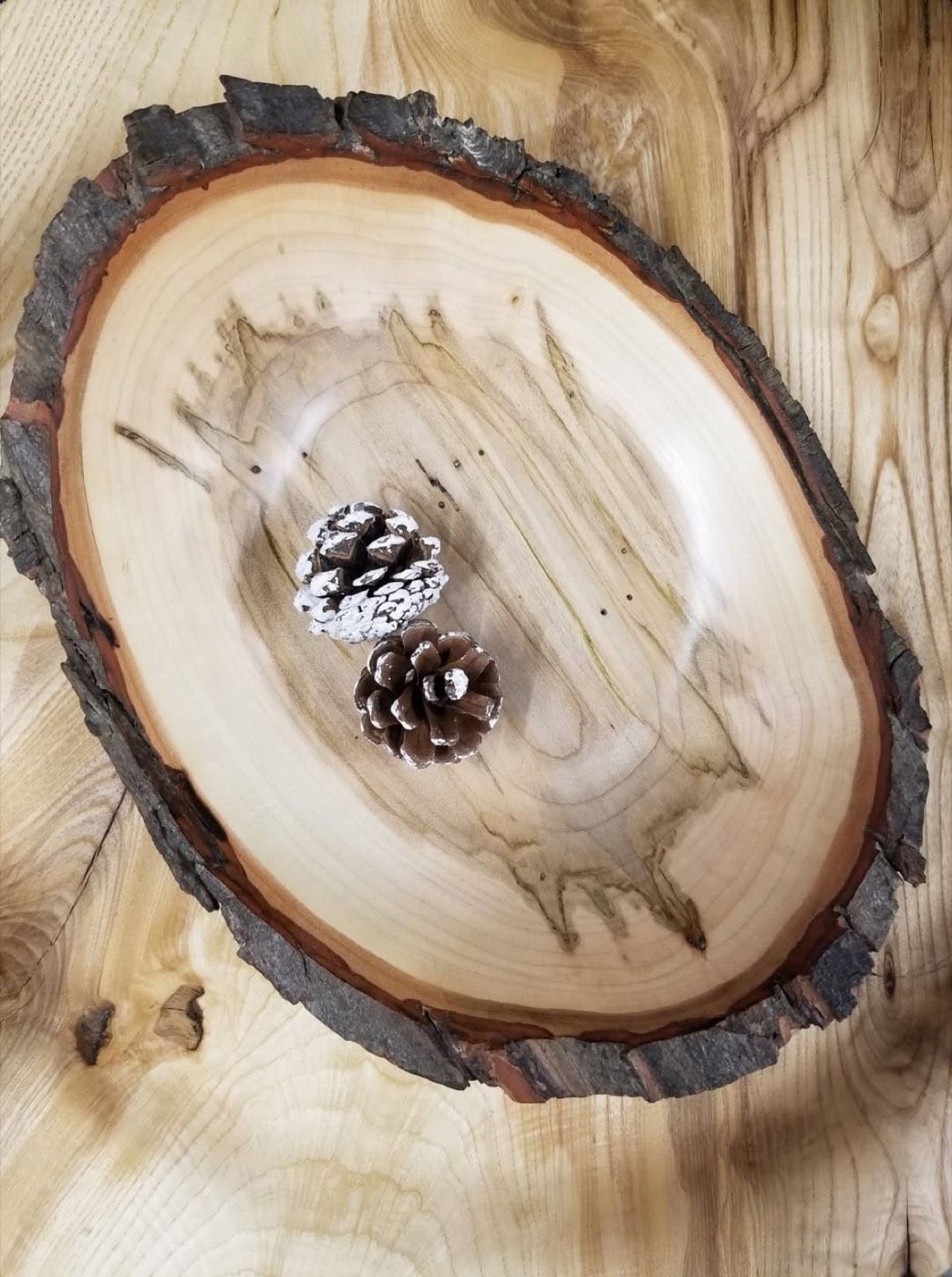 An oval live-edge ambrosia maple bowl with two pine cones